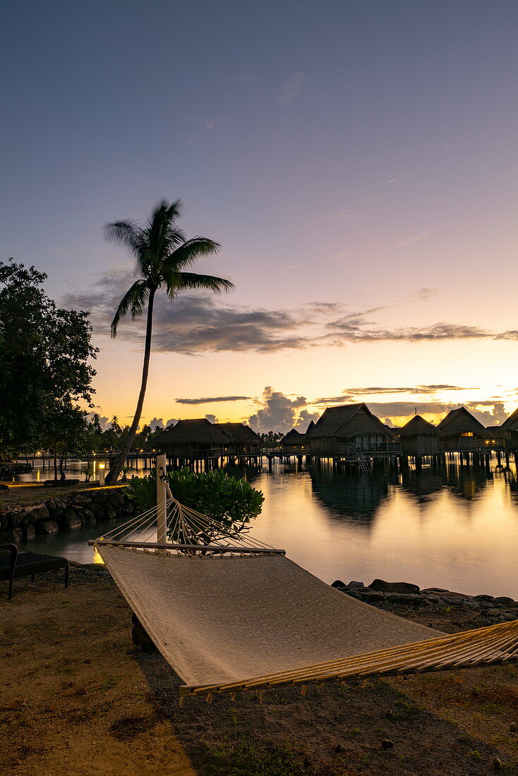 Hammock on the beach and overwater bungalows of the Sofitel Ia Ora Beach Resort in the Moorea Lagoon at daybreak, Moorea, Windward Islands, French Polynesia, South Pacific