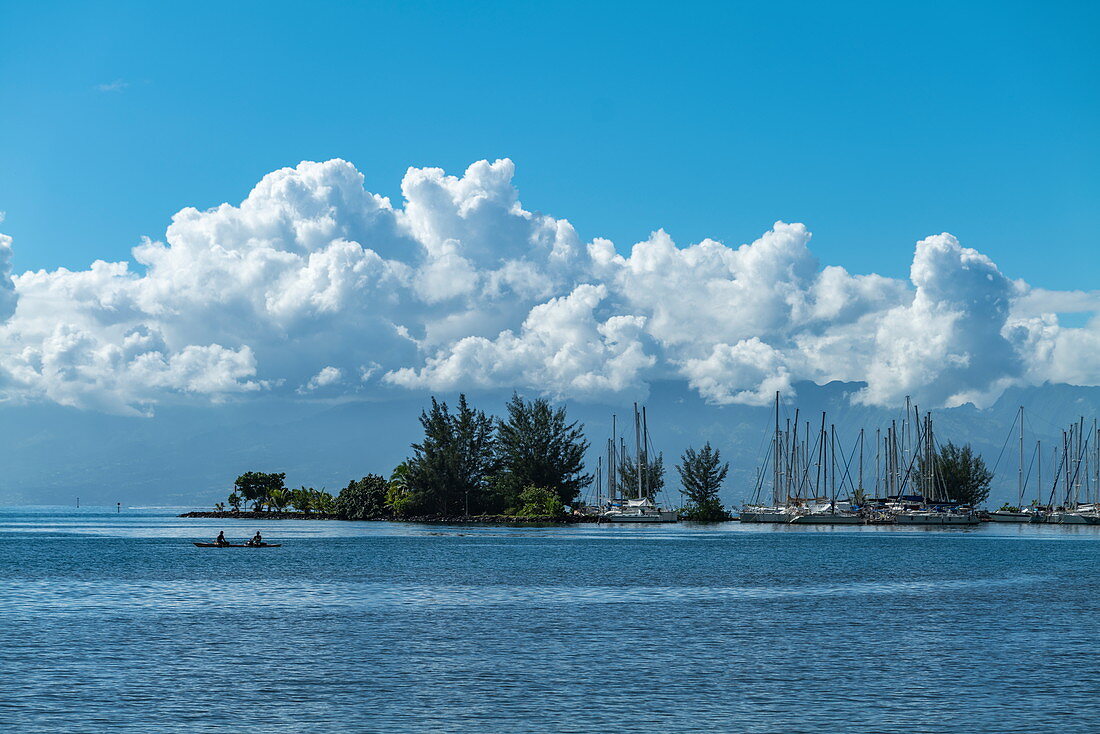 Two fishermen in canoes in the Moorea lagoon with sailboats in the marina behind them, Moorea, Windward Islands, French Polynesia, South Pacific