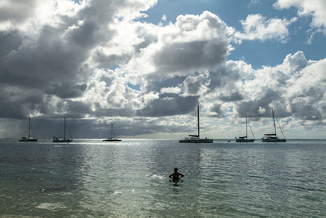 Silhouette eines Mannes im Wasser der Opunohu Bay mit Segelbooten vor Anker dahinter, Moorea, Windward Islands, Französisch-Polynesien, Südpazifik