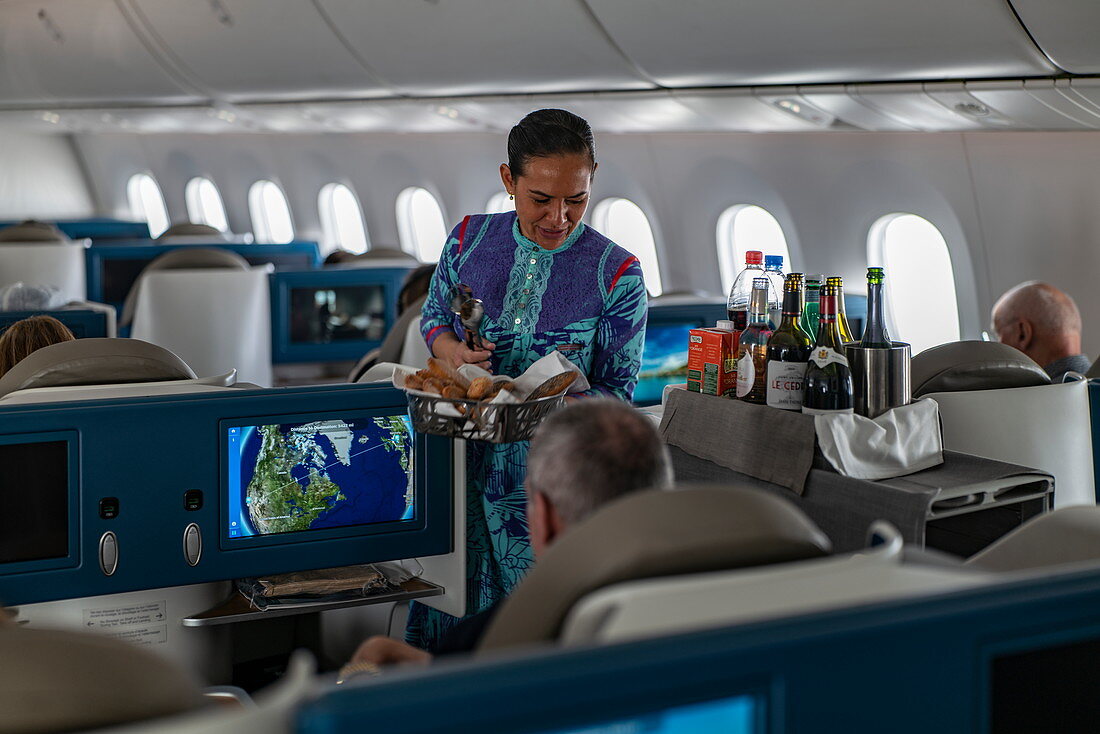 Flight attendant hands bread to passenger in Poerava Business Class aboard Air Tahiti Nui Boeing 787 Dreamliner aircraft on the flight from Paris Charles de Gaulle Airport (CDG) in France to Los Angeles International Airport (LAX) in the United States
