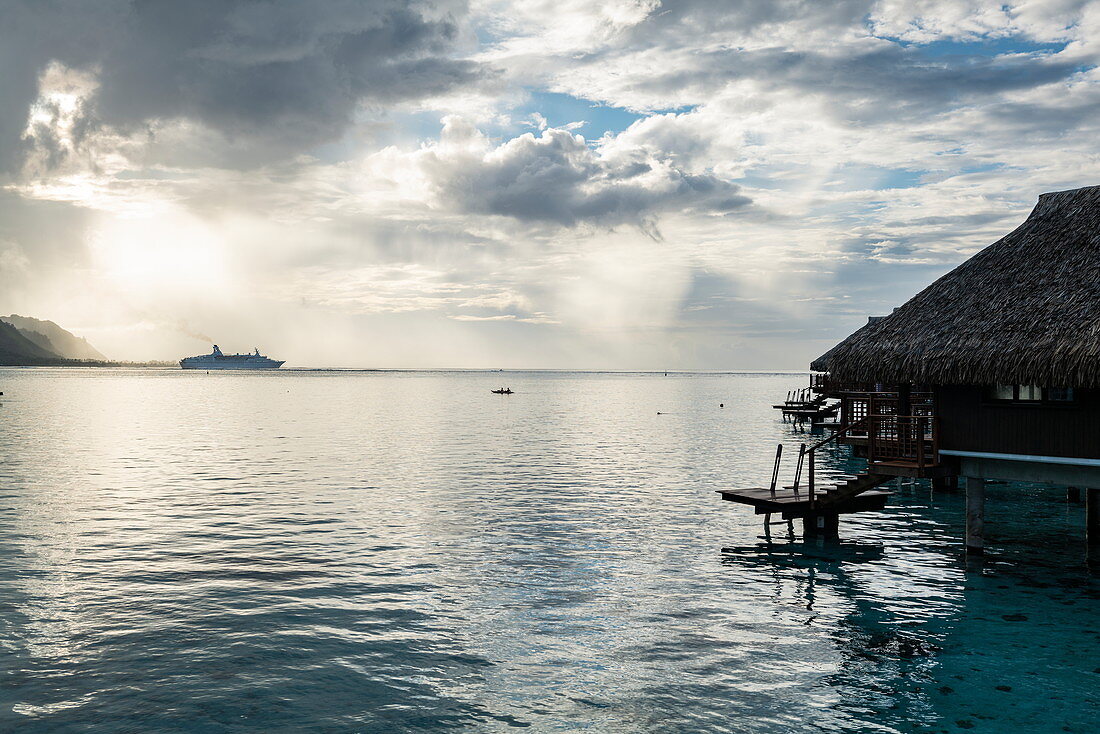 Kreuzfahrtschiff verlässt die Opunohu Bay während eines Gewitters mit Überwasserbungalows des Hilton Moorea Lagoon Resort & Spa, Moorea, Windward Islands, Französisch-Polynesien, Südpazifik