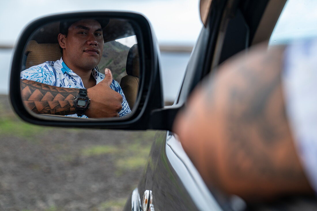 Daumen hoch: Ein Mann mit Tätowierungen auf dem Arm schaut in den Rückspiegel seines Allradfahrzeugs, Tekoapa, Ua Huka, Marquesas-Inseln, Französisch-Polynesien, Südpazifik