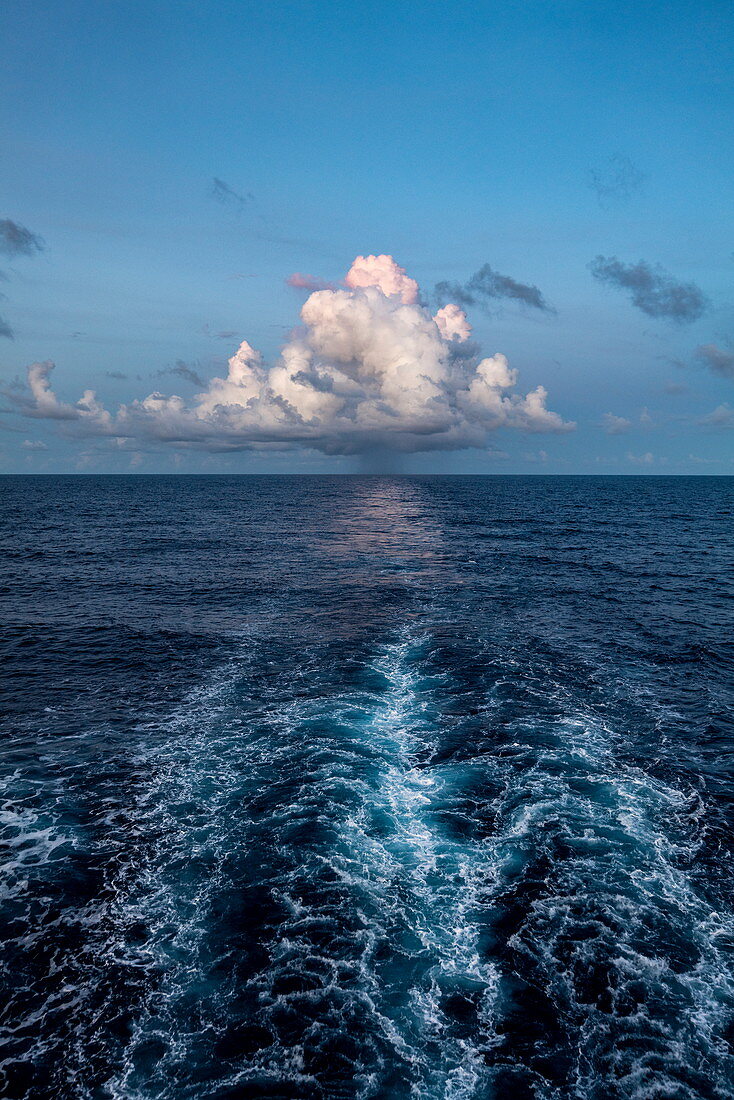 Wellen hinter Passagierfrachtschiff Aranui 5 (Aranui Cruises) mit einer majestätischen Wolke am Horizont, auf See zwischen den Marquesas-Inseln und den Tuamotu-Inseln, Französisch-Polynesien, Südpazifik