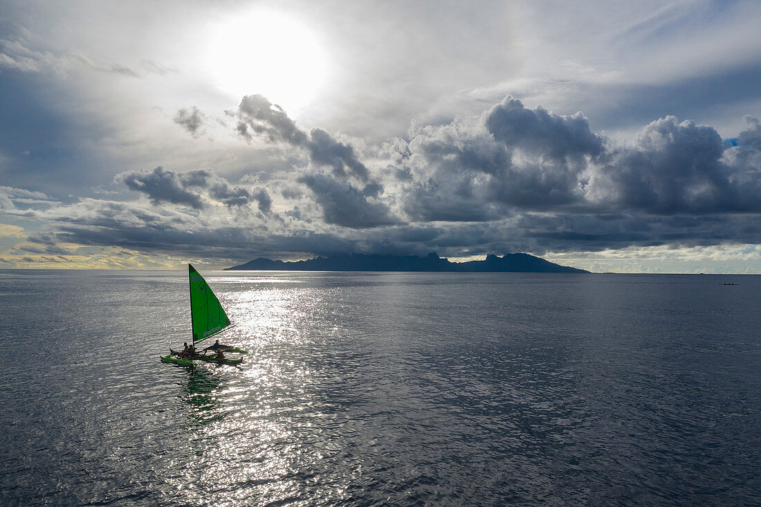 Luftaufnahme eines Ausleger Segelkanus bei Sonnenuntergang mit Insel Moorea in der Ferne, Nuuroa, Tahiti, Windward Islands, Französisch-Polynesien, Südpazifik