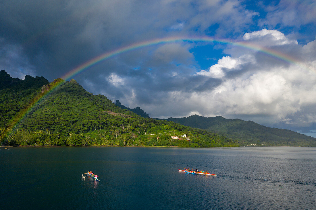 Aerial view of outrigger racing canoes in the Moorea Lagoon with rainbow and mountain backdrop, Avamotu, Moorea, Windward Islands, French Polynesia, South Pacific