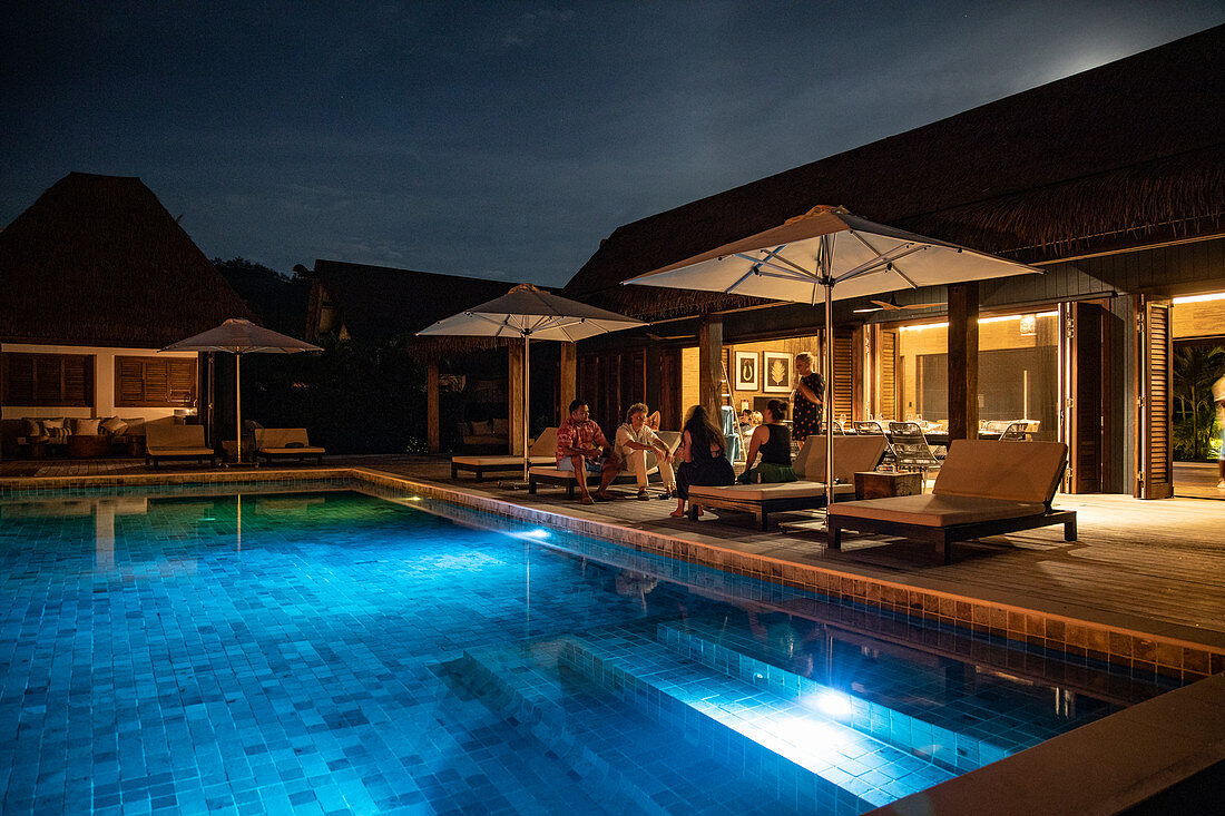 People relaxing by the private swimming pool of a residence villa accommodation at Six Senses Fiji Resort at night, Malolo Island, Mamanuca Group, Fiji Islands, South Pacific