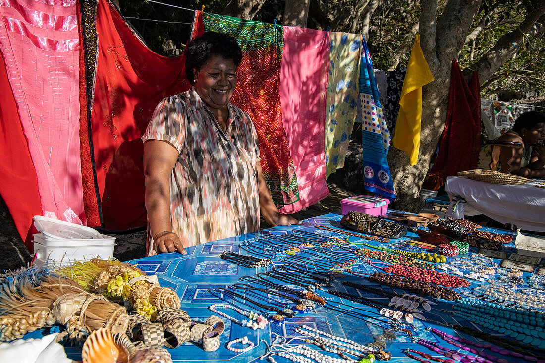 Lächelnde Frau mit Kunsthandwerk und Pareo Tüchern zum Verkauf an einem Souvenirstand am Strand, Sawa-i-Lau Island, Yasawa Group, Fidschi-Inseln, Südpazifik