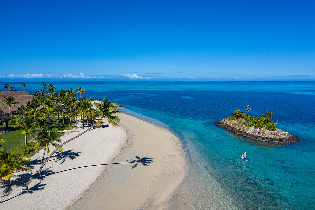 Luftaufnahme einer Residence Villa Unterkunft im Six Senses Fiji Resort mit Kokospalmen, Strand und einer Familie die Wassersport Aktivitäten neben kleiner vorgelagerter Insel genießt, Malolo Island , Mamanuca Group, Fidschi-Inseln, Südpazifik