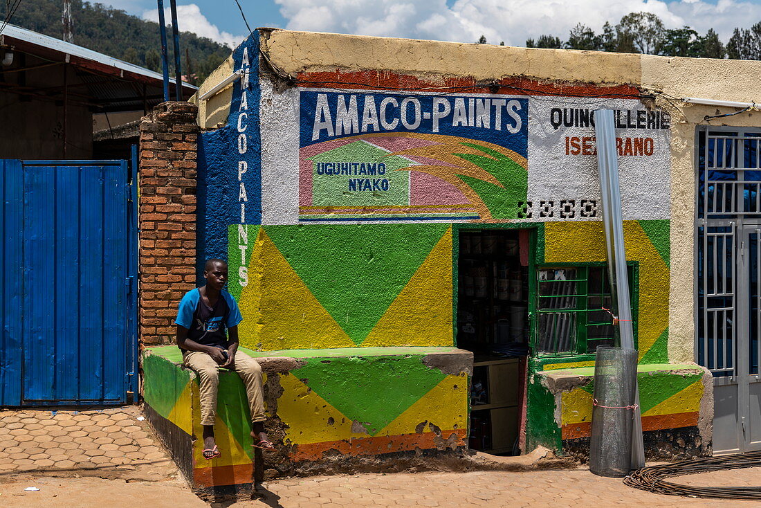 Young man sitting in front of a paint shop, Kigali, Kigali Province, Rwanda, Africa