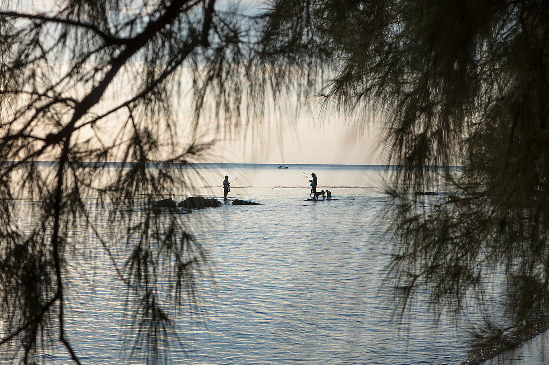 Silhouette of two fishermen and dogs standing on rocks in the water in front of Ong Lang Beach, Ong Lang, Phu Quoc Island, Kien Giang, Vietnam, Asia