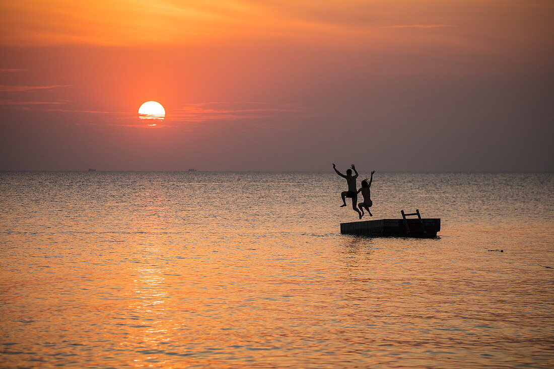 Silhouette von jungem Paar das bei Sonnenuntergang von einer Badeplattform vor dem Ong Lang Beach springt, Ong Lang, Insel Phu Quoc, Kien Giang, Vietnam, Asien