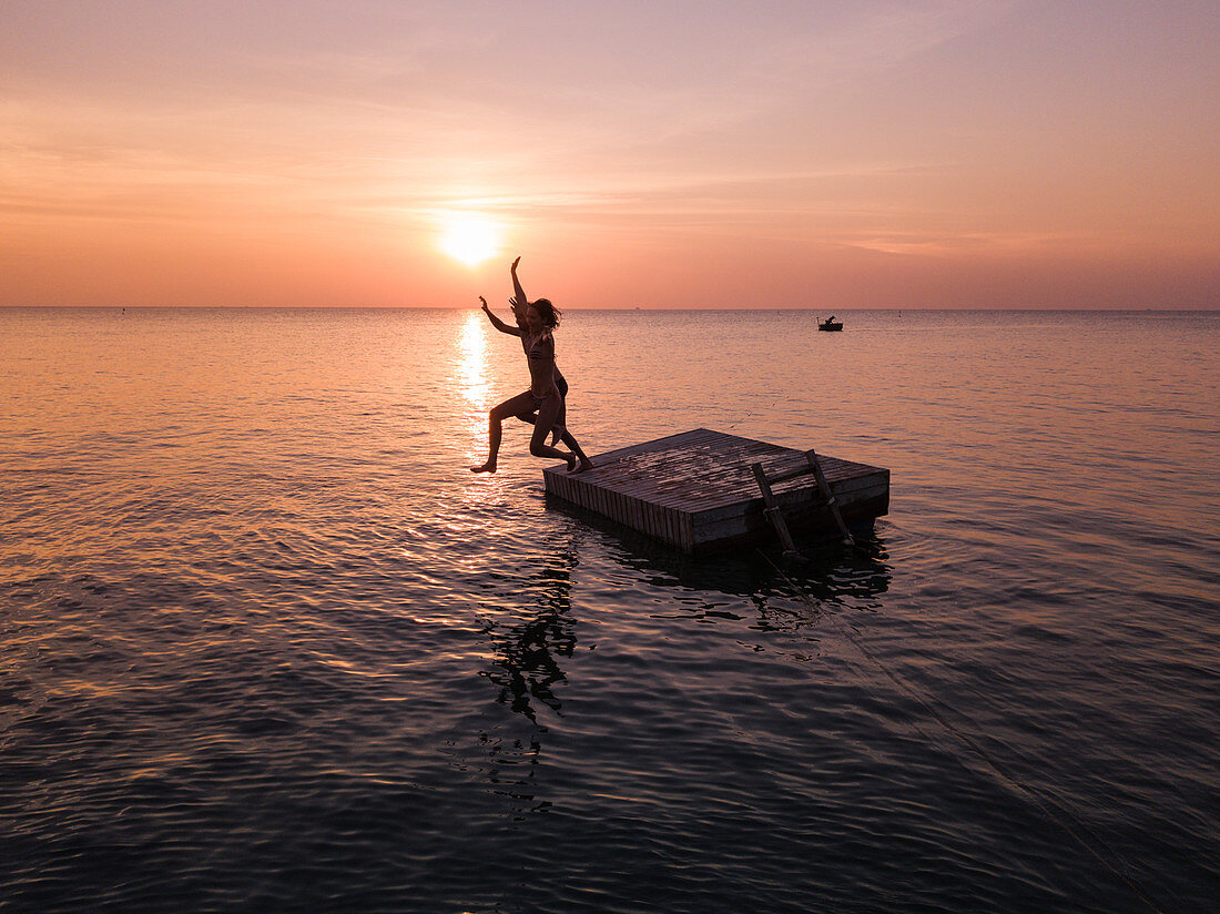 Aerial view silhouette of young couple jumping from a bathing platform at sunset on Ong Lang Beach, Ong Lang, Phu Quoc Island, Kien Giang, Vietnam, Asia