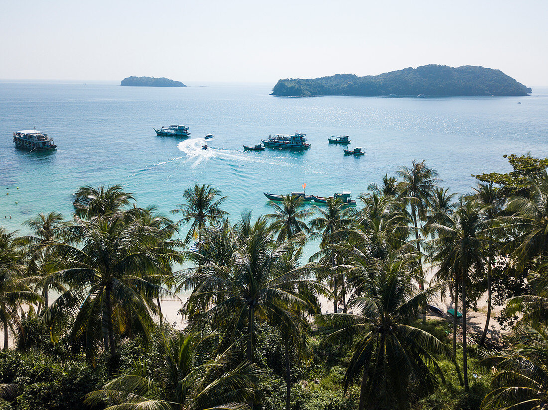 Luftaufnahme von Kokospalmen nahe Strand mit Ausflugsbooten, Fischerbooten und Inseln in der Ferne, May Rut Island, nahe Insel Phu Quoc, Kien Giang, Vietnam, Asien