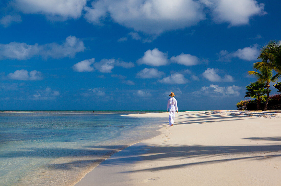 Frau in weißer tropischer Kleidung geht an einem unberührten Strand entlang. Antigua, Westindische Inseln.