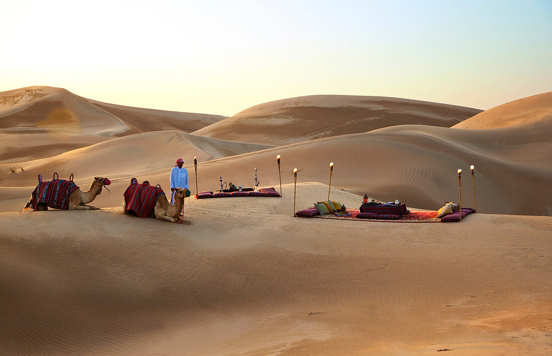 Ein wunderschönes Wüstenpicknick inmitten von Sanddünen Kamele und Betreuer im Vordergrund. Saudi-Arabien, Vorderasien