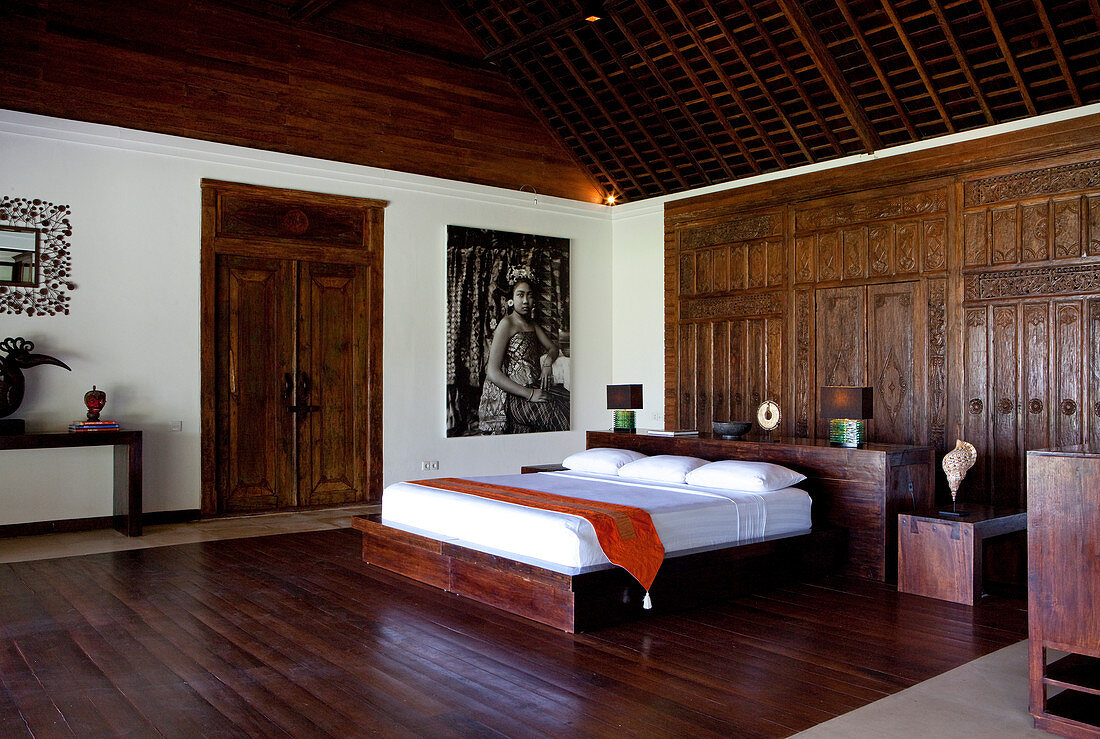 Eine Innenaufnahme eines in Hartholz entworfenen und gebauten Bali-Schlafzimmers mit einer geschnitzten Tür als Kopfteil, Bali, Indonesien, Asien