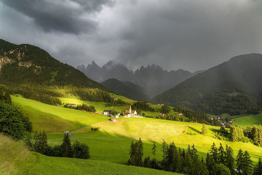 Sunlight through storm clouds over the Odle and village of Santa Magdalena, Val di Funes, South Tyrol, Dolomites, Italy