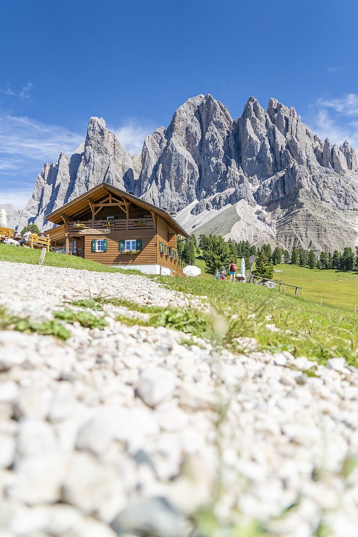Hikers resting at Malga Casnago (Gschnagenhardt) hut at feet of the Odle mountains, Val di Funes, South Tyrol, Dolomites, Italy