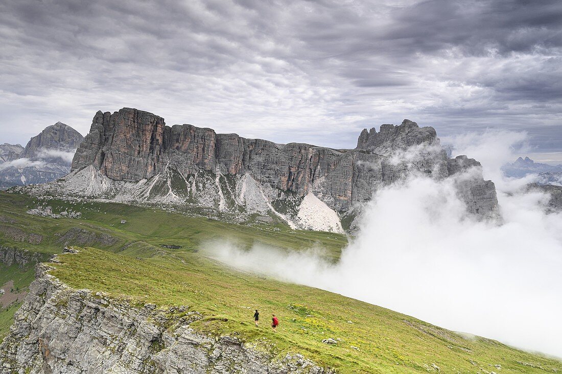Wanderer steigen vom Berg Mondeval ab, während schnelle und dichte Wolken aus dem Tal aufsteigen, in der Mitte der Lastoi Di Formin, im Hintergrund links der Tofana di Rozes