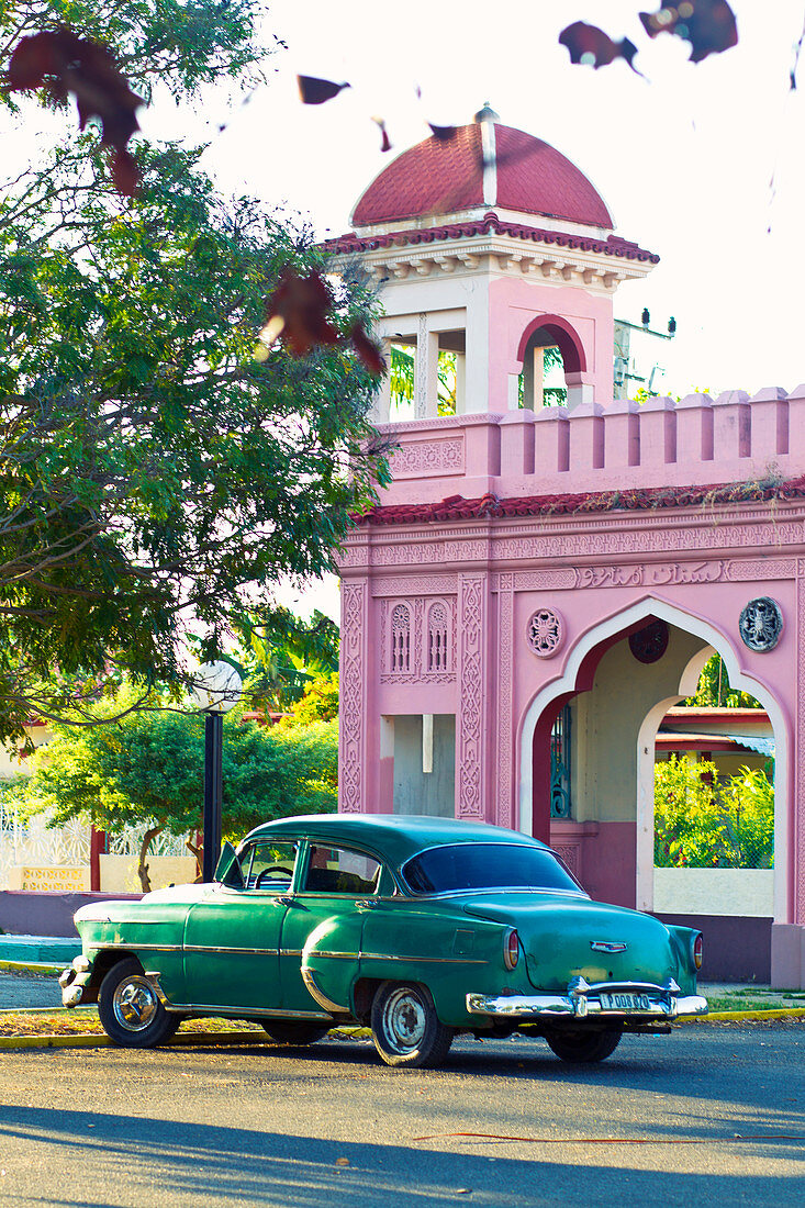Classic green car in front of a pink gateway in Arabic style in Cienfuegos, Cuba