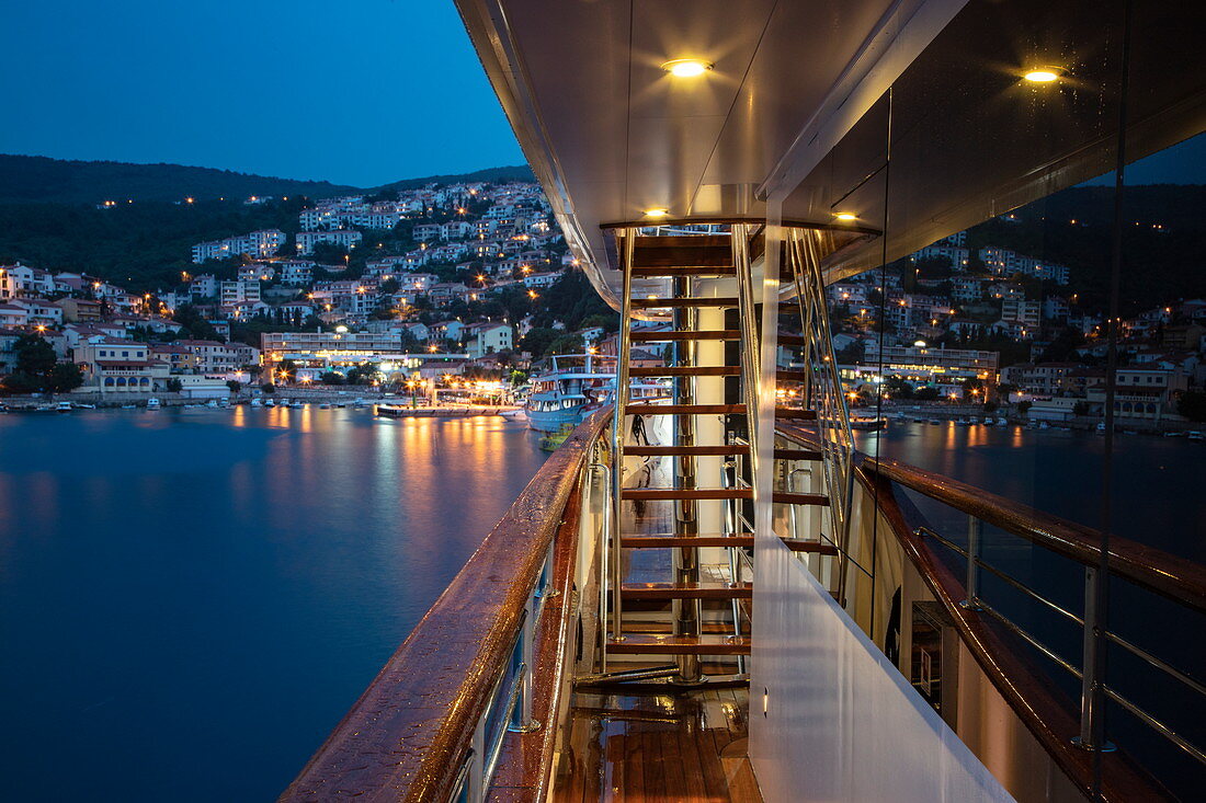 Deck von Kreuzfahrtschiff mit Stadt dahinter in der Abenddämmerung, Rabac, Istrien, Kroatien, Europa
