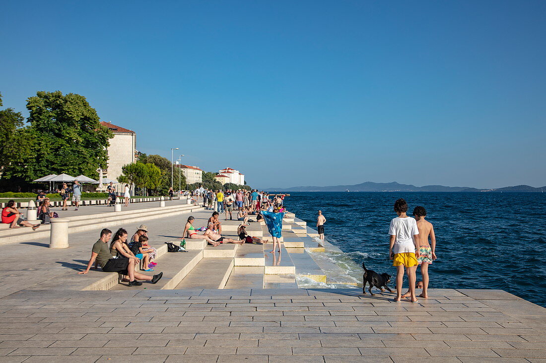 Menschen entspannen sich an der Strandpromenade und lauschen der Meeresorgel, Zadar, Zadar, Kroatien, Europa
