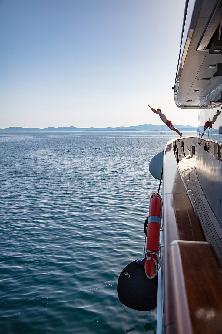 Man jumps from the deck of the cruise ship into the water to enjoy a swim in a pristine bay, near Kukljica, Zadar, Croatia, Europe