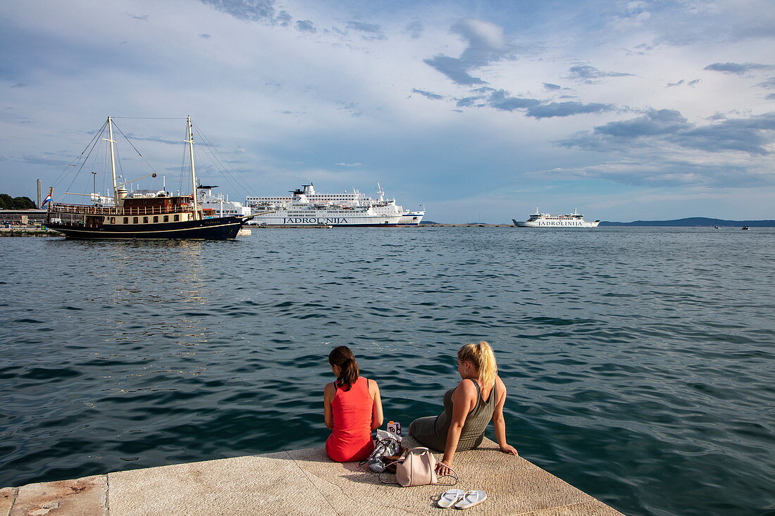 Two young women relax along the seafront promenade with ships in the harbor, Split, Split-Dalmatia, Croatia, Europe