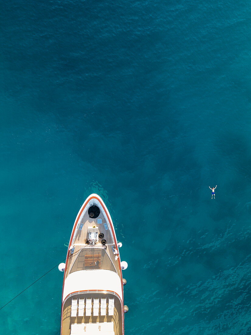 Luftaufnahme von Kreuzfahrtschiff mit Mann der neben dem Bug im Wasser schwimmt, nahe Kampor, Primorje-Gorski Kotar, Kroatien, Europa