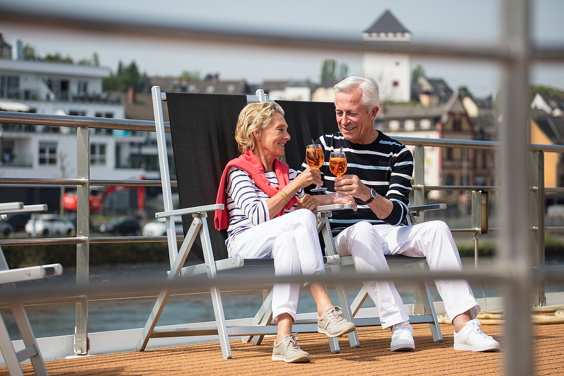 Paar genießt Cocktails auf Sonnendeck von Flusskreuzfahrtschiff während einer Kreuzfahrt auf dem Rhein, nahe Andernach, Rheinland-Pfalz, Deutschland, Europa