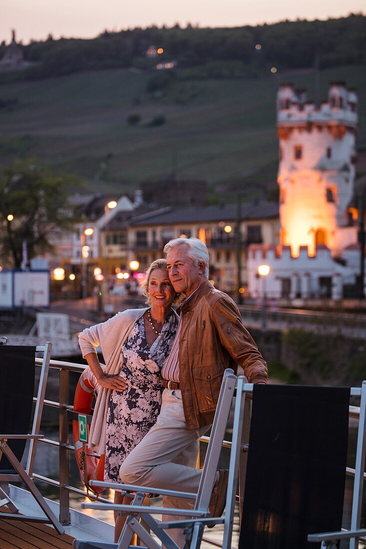 Paar auf Sonnendeck von Flusskreuzfahrtschiff  während einer Kreuzfahrt auf dem Rhein in der Abenddämmerung, Rüdesheim am Rhein, Hessen, Deutschland, Europa