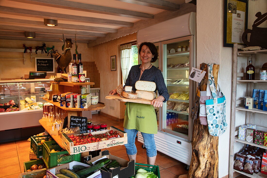 Friendly woman with cheese for sale in the farm shop at the ecological farm Der Berghof, Schöllkrippen, Kahlgrund, Spessart-Mainland, Franconia, Bavaria, Germany, Europe