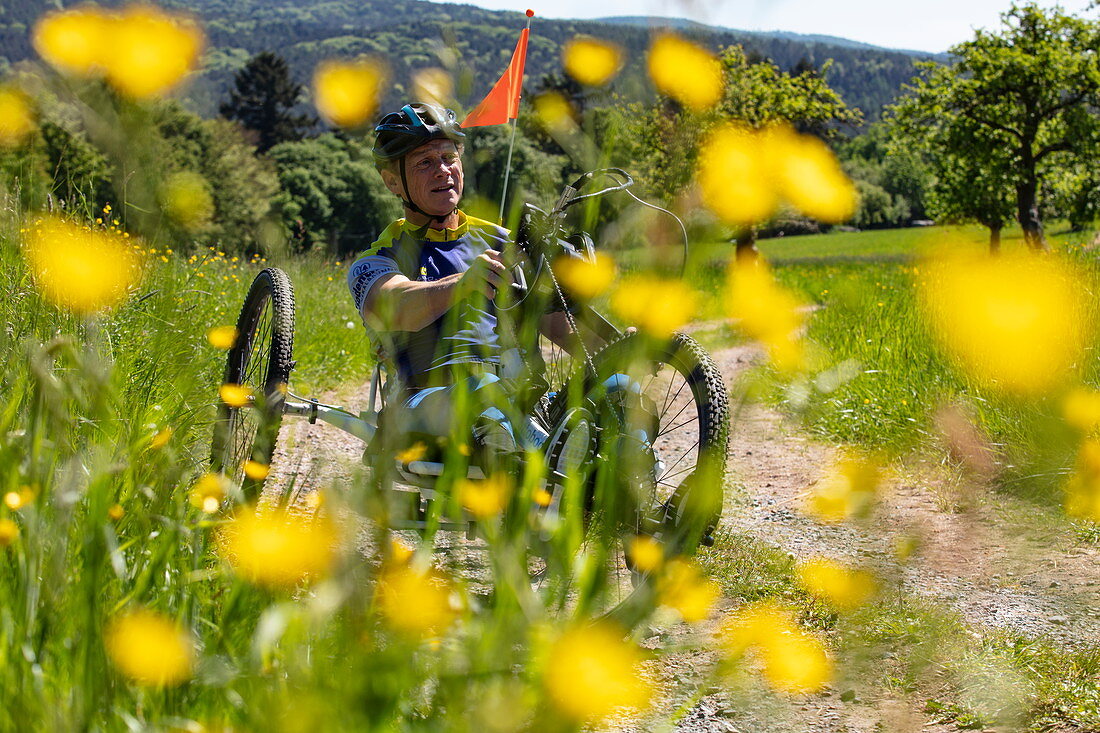Man rides a bicycle for paraplegics on a dirt road through lush spring meadow, Heimbuchenthal, Räuberland, Spessart-Mainland, Franconia, Bavaria, Germany, Europe
