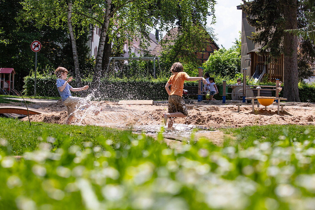 Zwei Jungen haben Spaß und bespritzen sich mit Wasser auf einem städtischen Spielplatz, Tauberbischofsheim, Baden-Württemberg, Deutschland, Europa