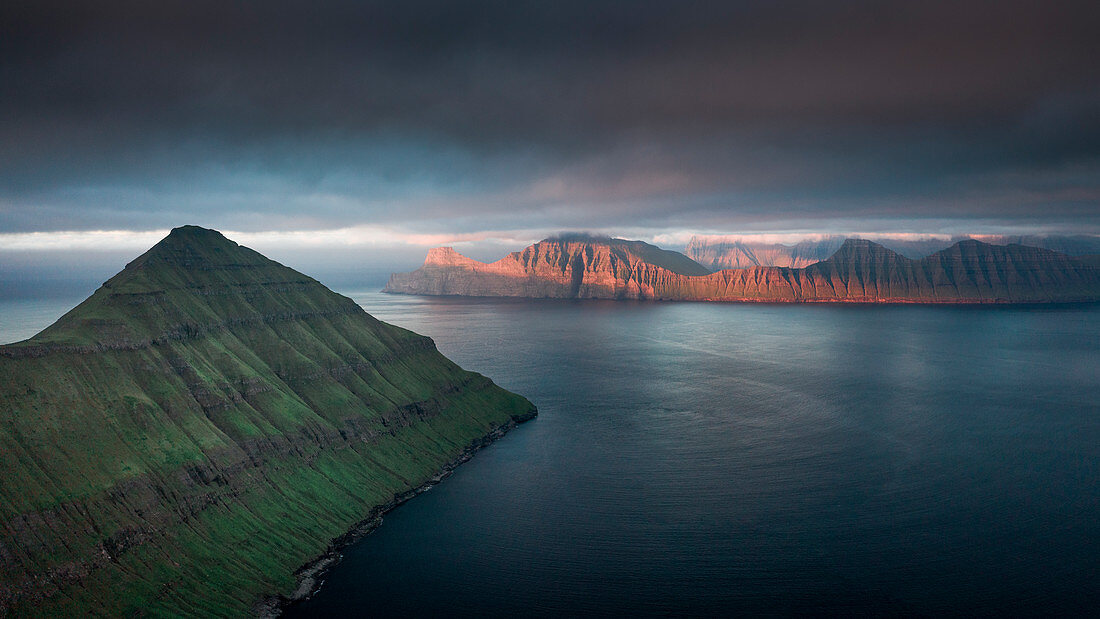 Ausblick vom Hvithamar nahe dem Ort Gjogv auf der Färöer Insel Eysturoy mit Panoramablick über Fjord Richtung Kalsoy bei Sonnenuntergang\n