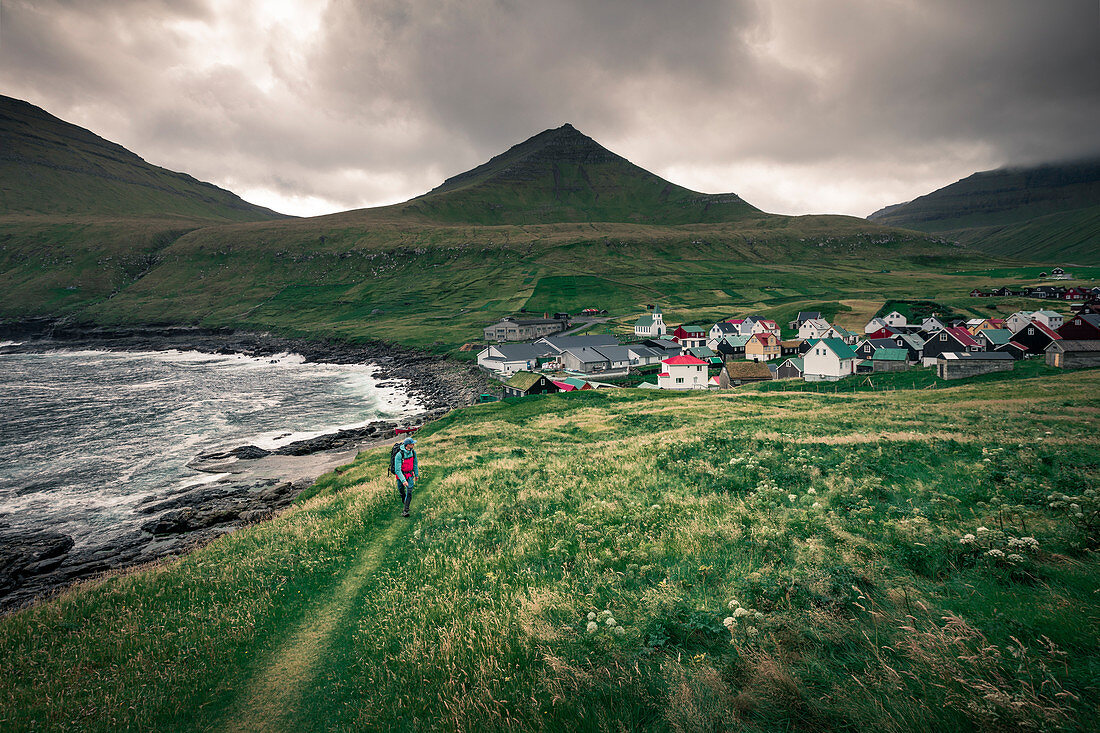 Man walks on path in front of the village of Gjogv on Eysteroy, Faroe Islands