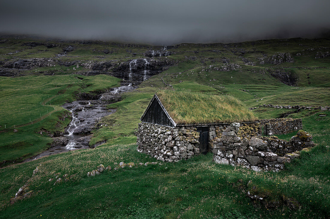 Huts with a grass roof and waterfall in Saksun village on Streymoy Island, Faroe Islands