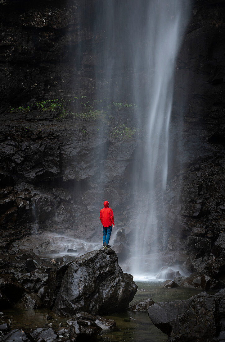 Mann mit roter Jacke am Wasserfall Fossa auf Insel Streymoy, Färöer Inseln\n