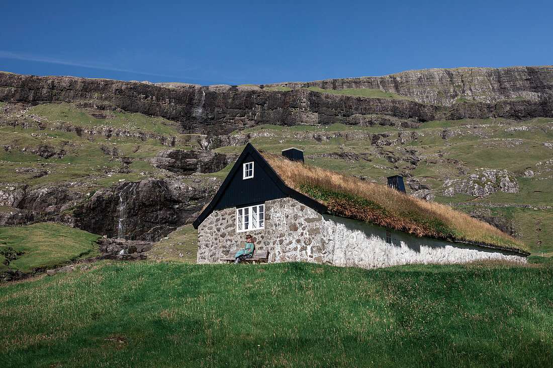 Woman in front of a hut with a grass roof in the village of Saksun on the island of Streymoy, Faroe Islands