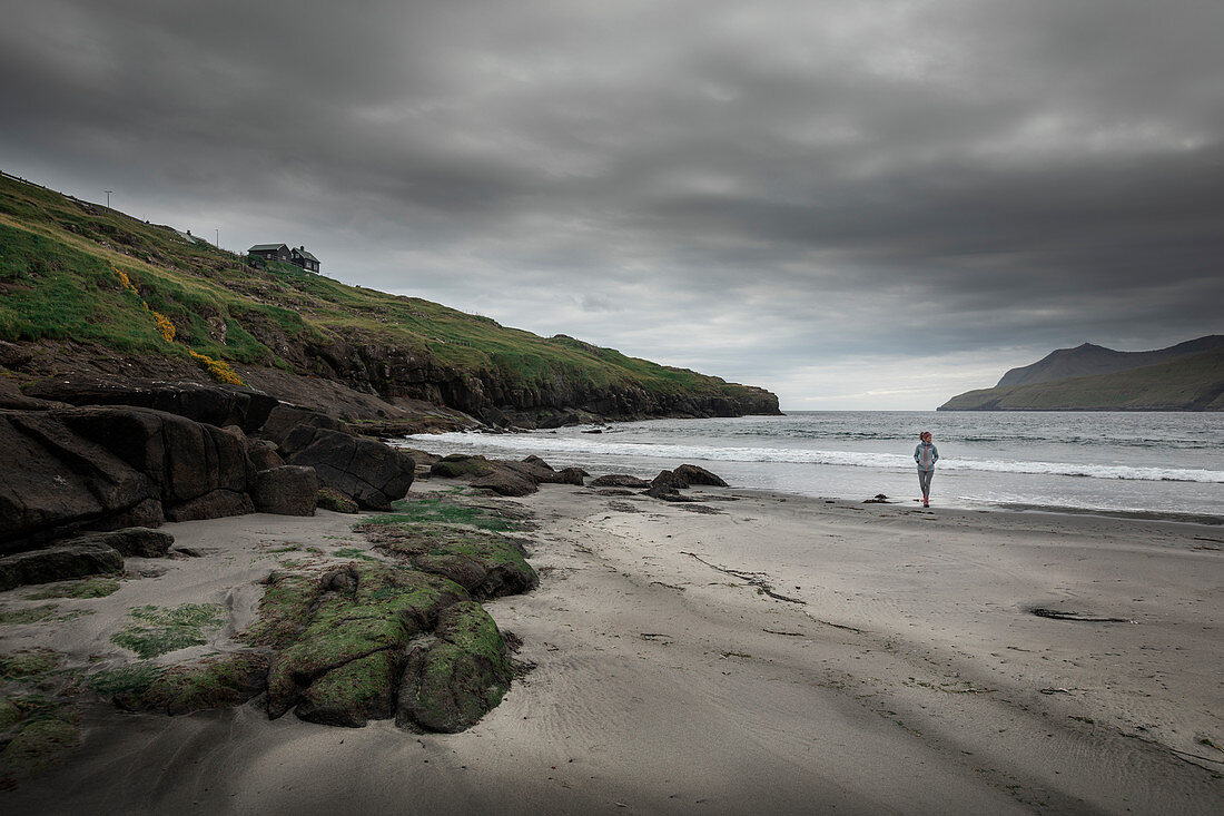 Woman runs in the sandy bay of Leynar on Streymoy, Faroe Islands