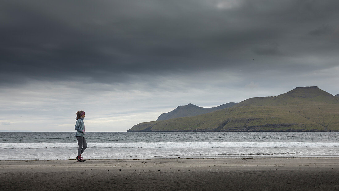 Woman runs in the sandy bay of Leynar on Streymoy, Faroe Islands