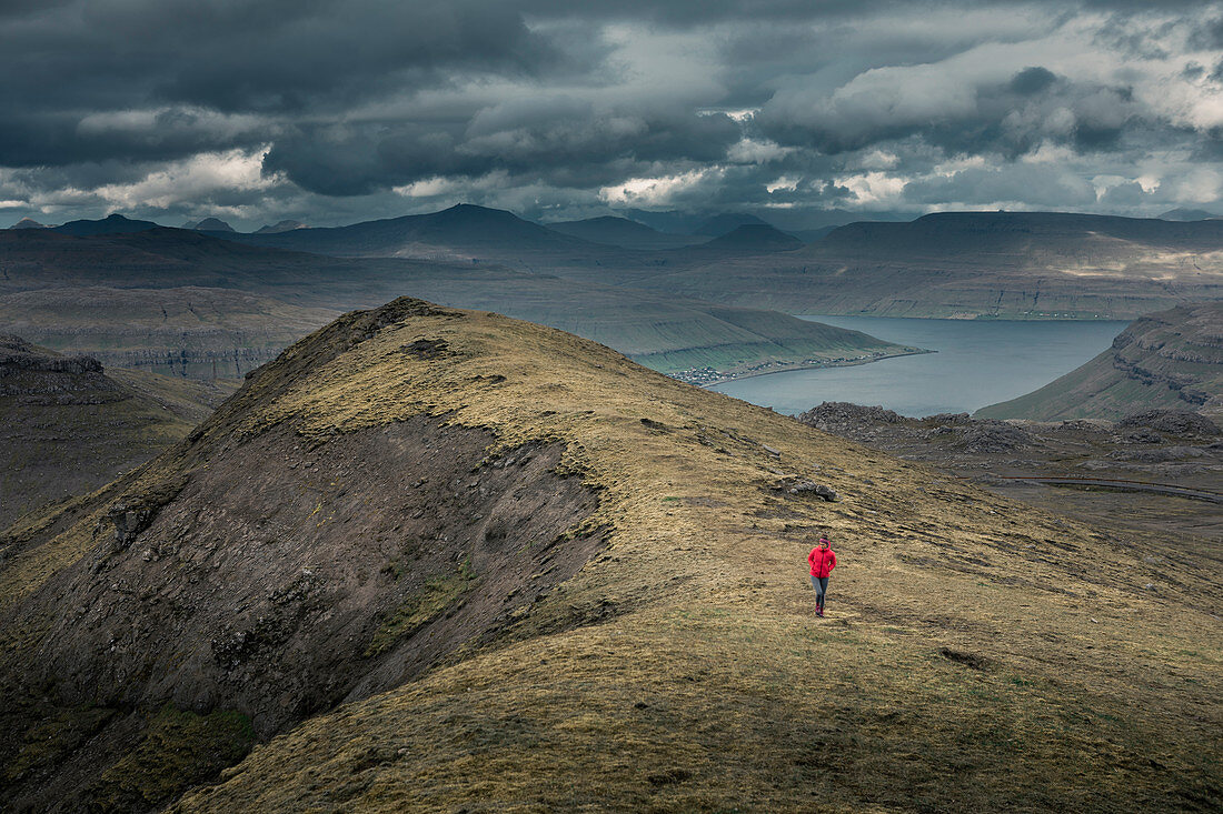 Woman hiking in the Faroe Islands landscape under dramatic clouds