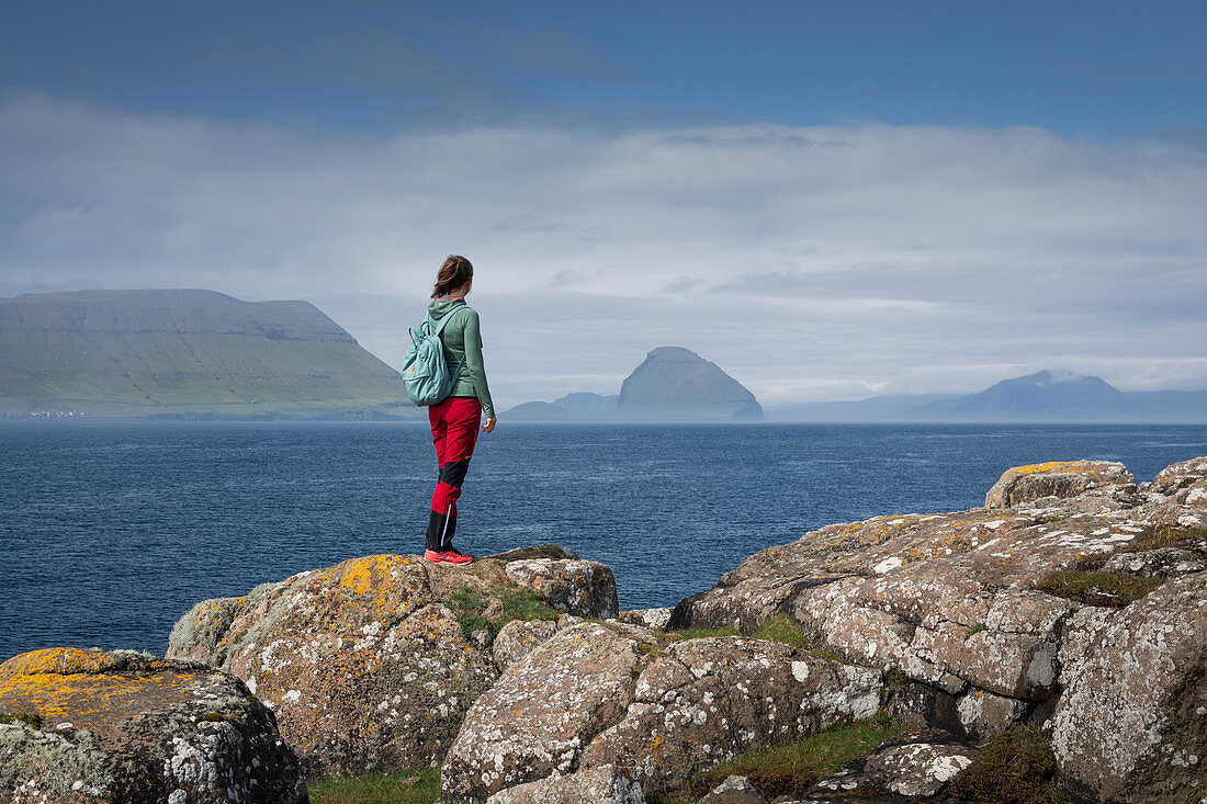 Woman on the coast overlooking islands of the Faroe Islands in sunshine