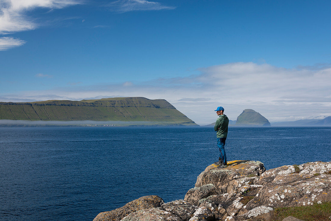 Mann an der Küste mit Blick auf Inseln der Färöer Inseln bei Sonne\n