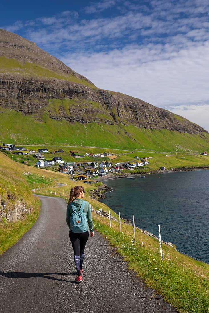 Frau wandert bei Sonnenschein beim Dorf Bour auf Vagar, Färöer Inseln\n