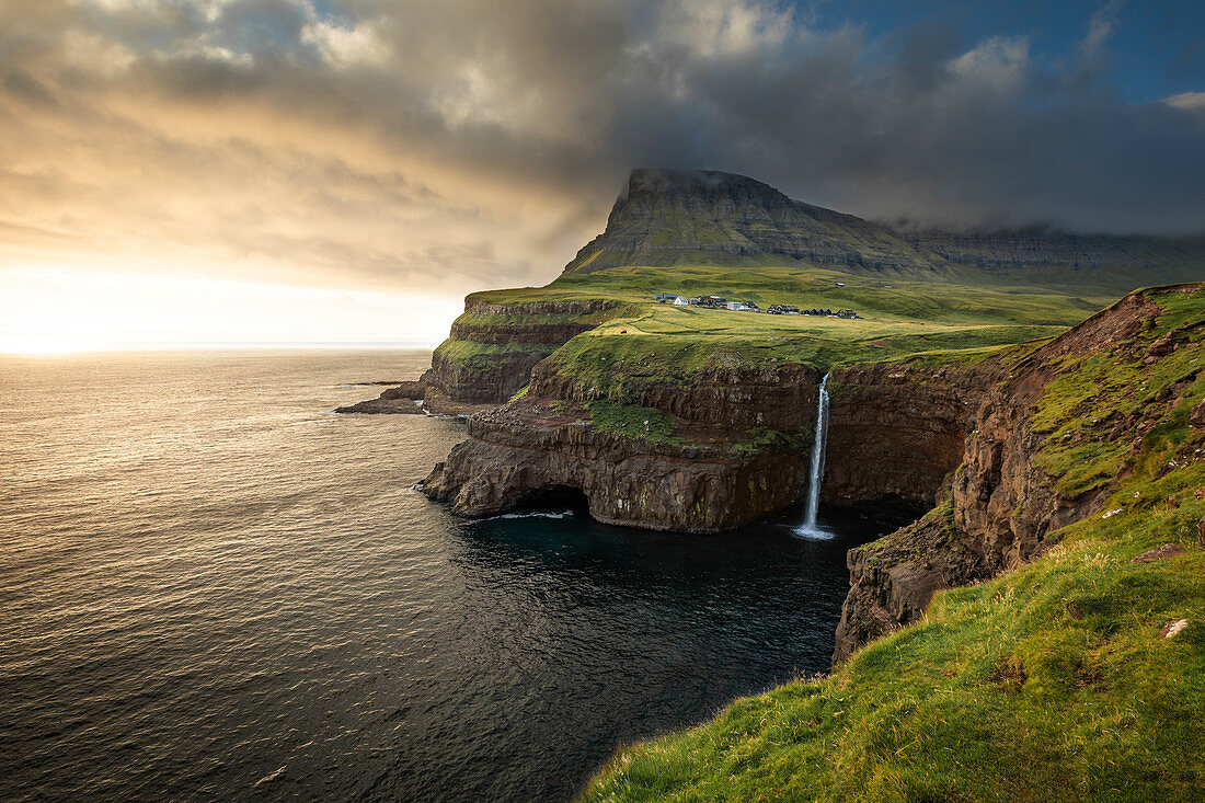 Sunset at the Múlafossur waterfall with the village of Gásadalur on the island of Vagar, Faroe Islands