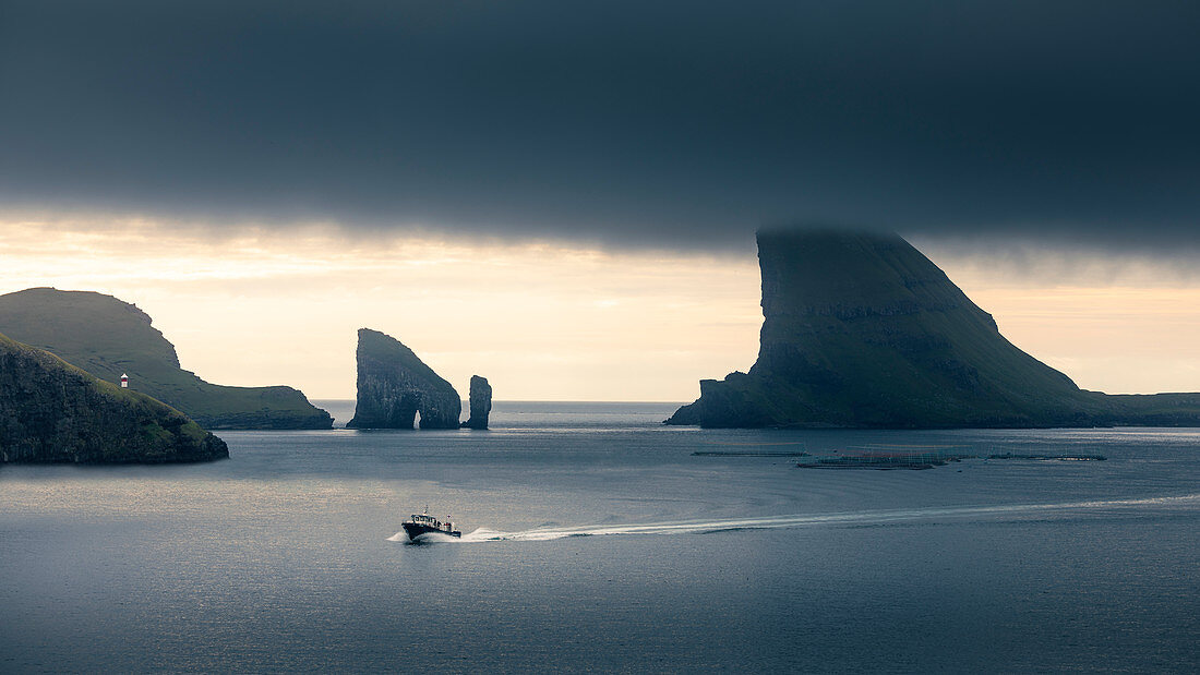 Boat in front of rock formations of Drangarnier and Tindholmur island in sunset on Vagar, Faroe Islands