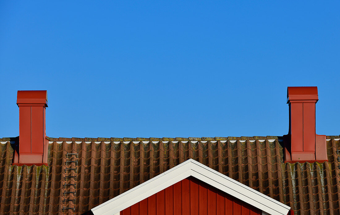 Ansicht eines roten Schwedenhauses vor blauem Himmel mit zwei Schornsteinen, Grimsholmen, Halland, Schweden
