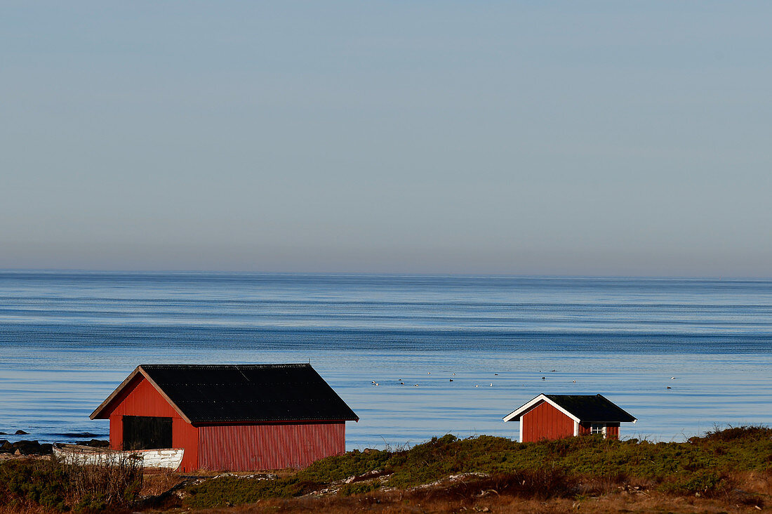 Rote Fischerhütten und ein Boot am Meer bei Grimsholmen, Hallandslän, Schweden