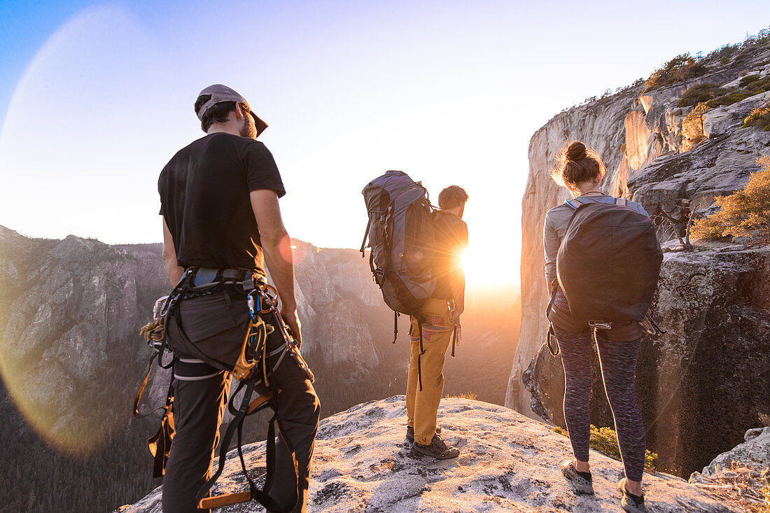 Eine Gruppe von Menschen auf einem Felsvorsprung beobachtet einen Sonnenuntergang.